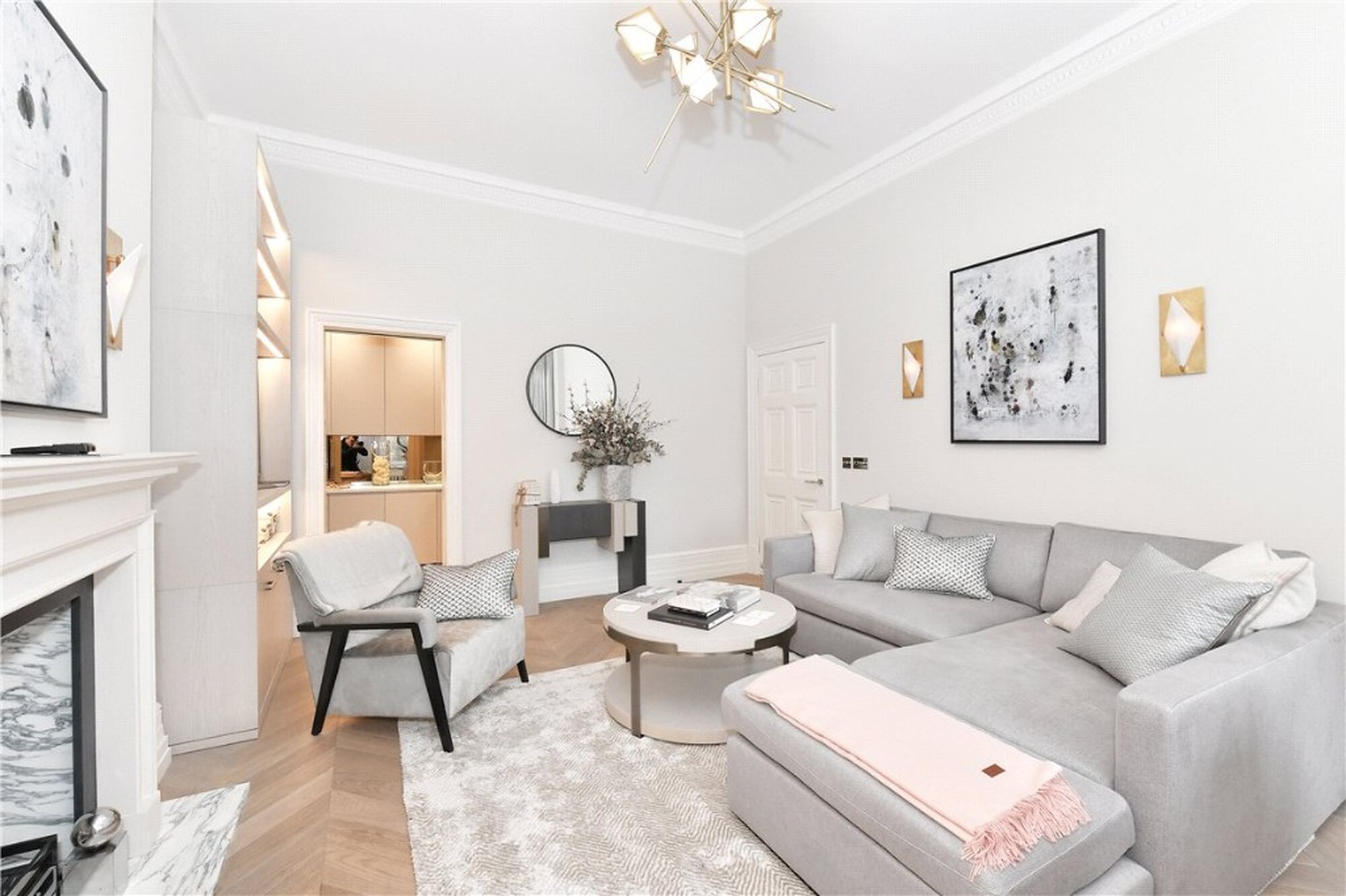 Open-plan sitting room in a Mount Street apartment with grey sofa, chandelier and view to the kitchen